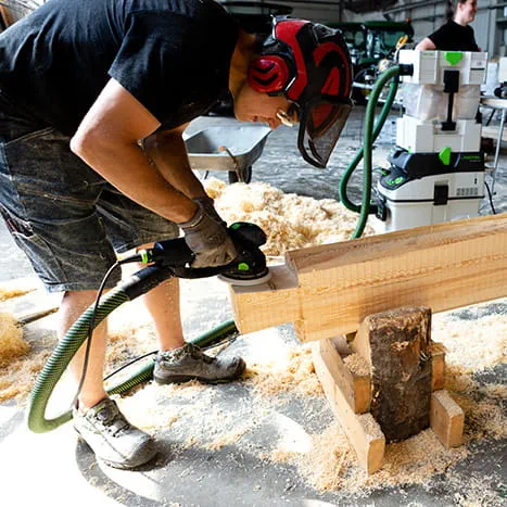 Eine Saunabauerin beim Schleifen einer Holzoberfläche mit dem Rotex 150 von Festool.